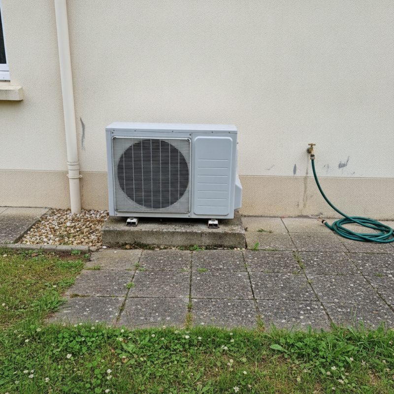 Groupe extérieur de climatisation posé au sol contre un mur de maison